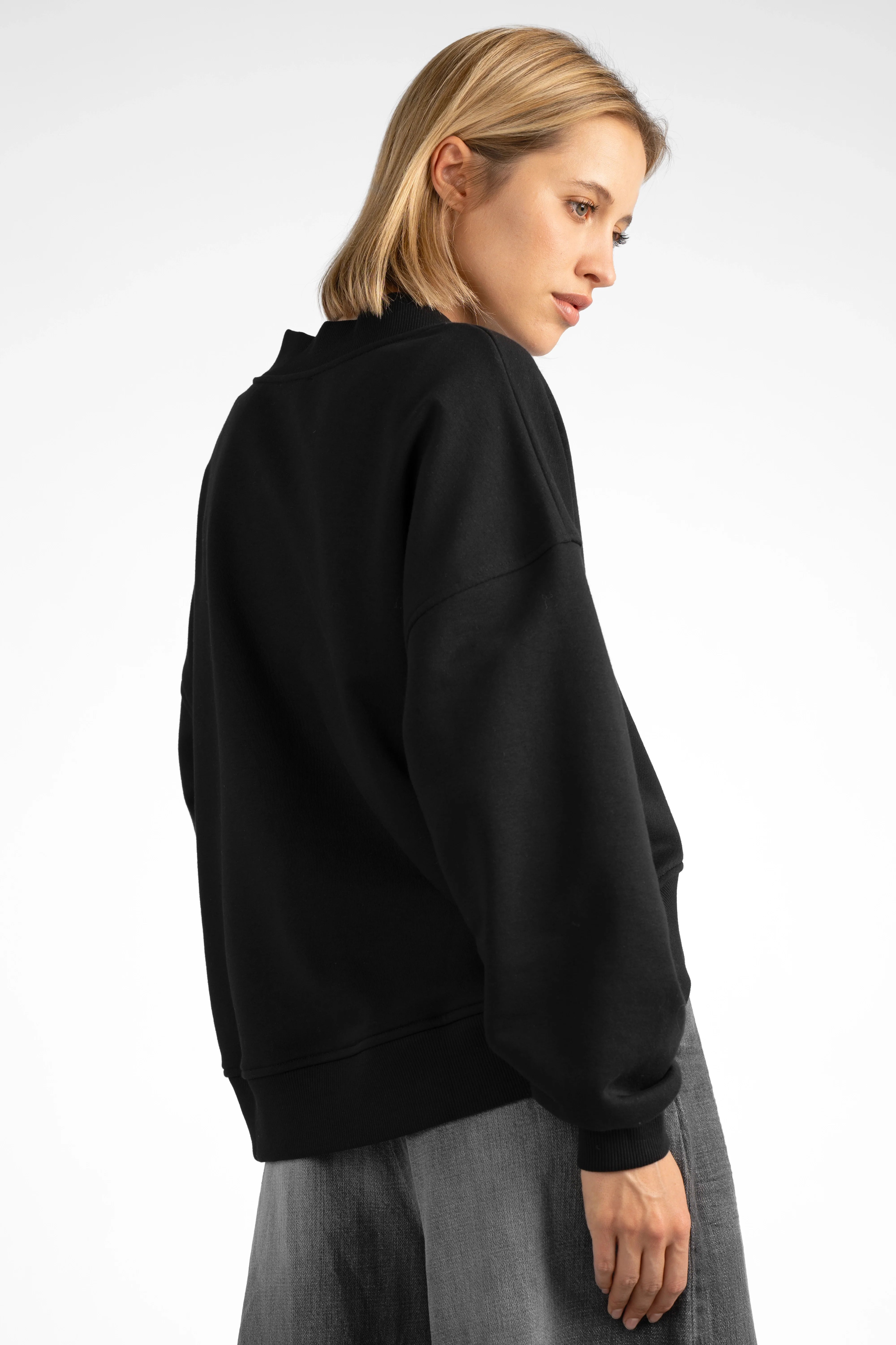 Woman wearing black SEREA Sweater mit V-Ausschnitt with relaxed fit and ribbed cuffs, shown from the back.