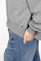 Close-up of grey SEREA Sweater with ribbed cuffs and hem, worn with blue jeans.