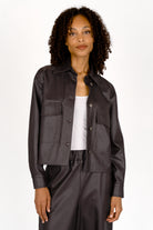 Woman wearing cropped black eco-leather shirt jacket with Kent collar and large chest pockets