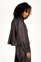 Side view of a woman wearing a cropped, supersoft eco-leather shirt jacket with Kent collar and chest pockets