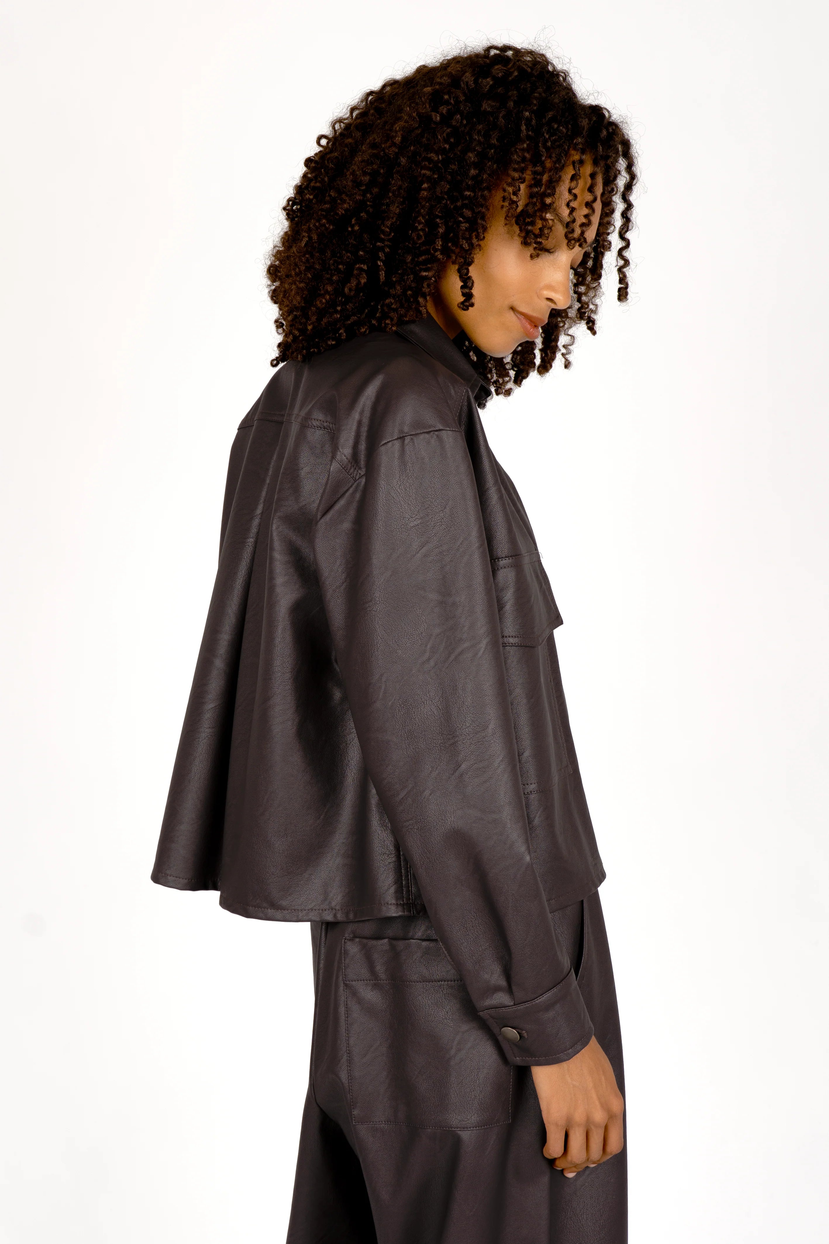Side view of a woman wearing a cropped, supersoft eco-leather shirt jacket with Kent collar and chest pockets
