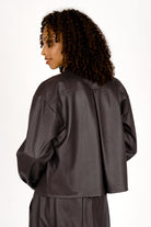 Back view of a woman wearing a cropped, supersoft eco-leather Hemdjacke with slightly dropped shoulders and Kent collar.