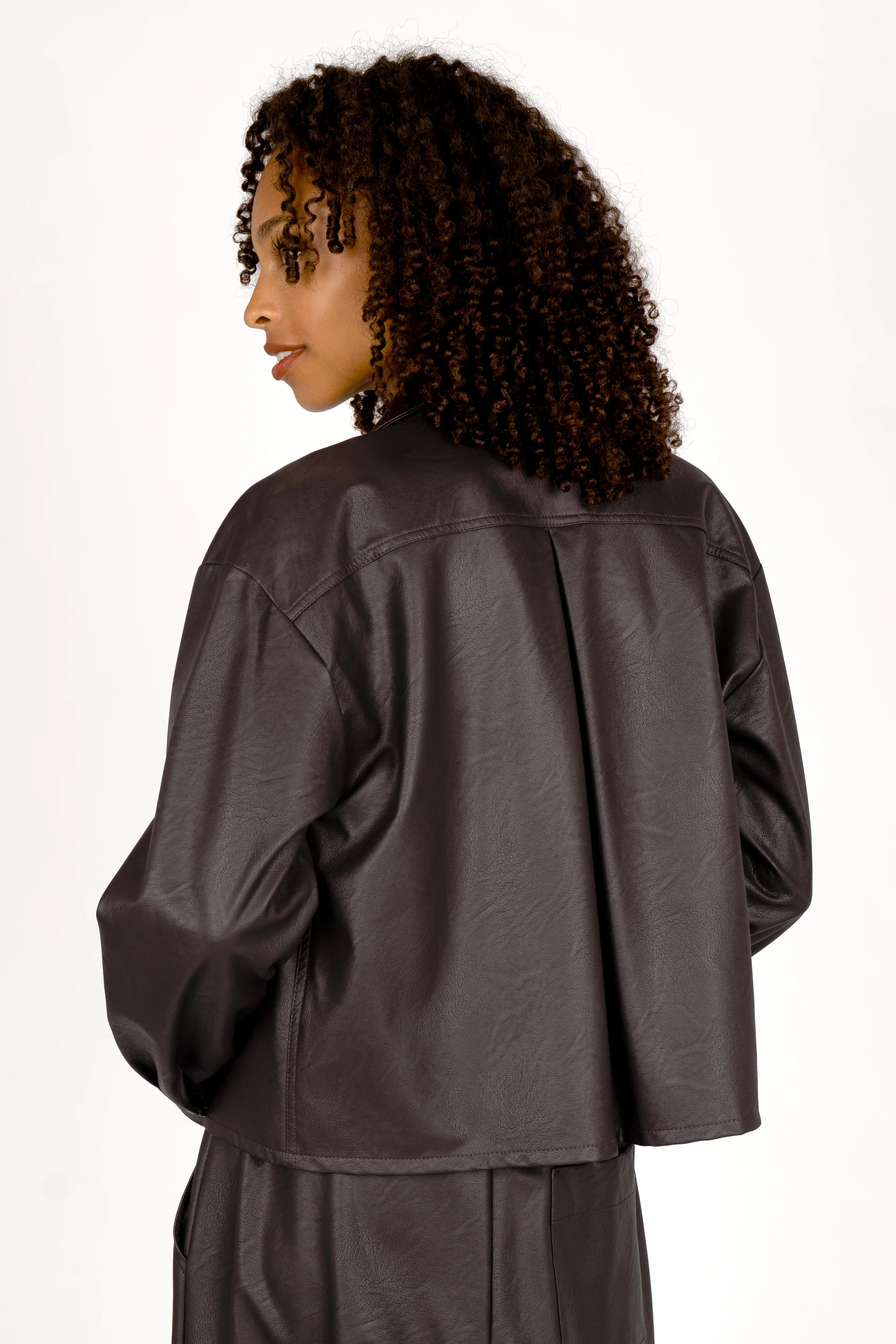Back view of a woman wearing a cropped, supersoft eco-leather Hemdjacke with slightly dropped shoulders and Kent collar.