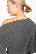 Frau trägt graues One-Shoulder Top aus plissiertem Kreppjersey mit weitem Fledermausärmel und asymmetrischem Schnitt