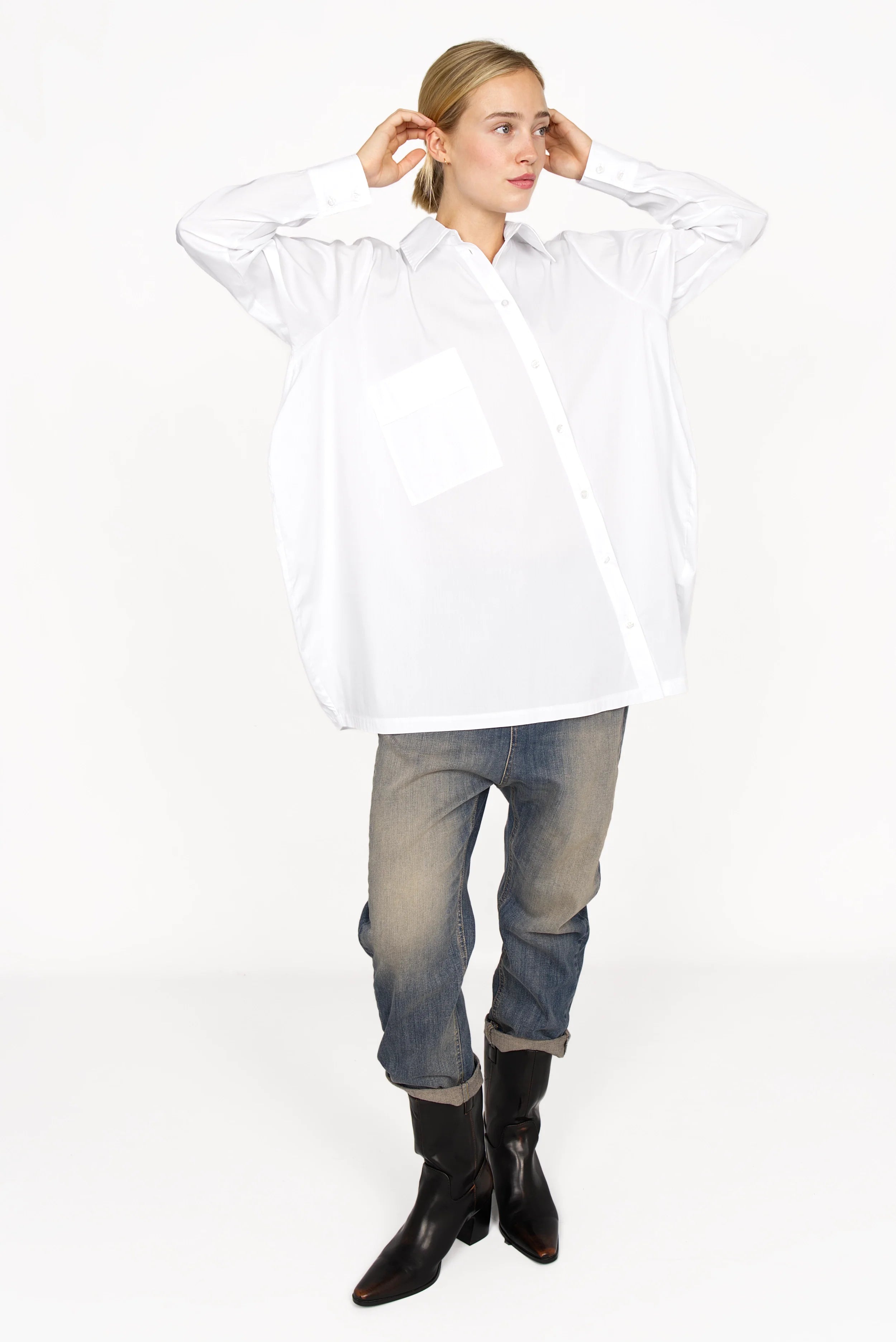 Woman wearing a white oversized Hemdbluse with asymmetrical button placket, long sleeves, and a classic collar.