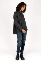 Woman wearing black oversized Bluse with classic collar, button front, and dropped shoulders paired with blue jeans and black boots