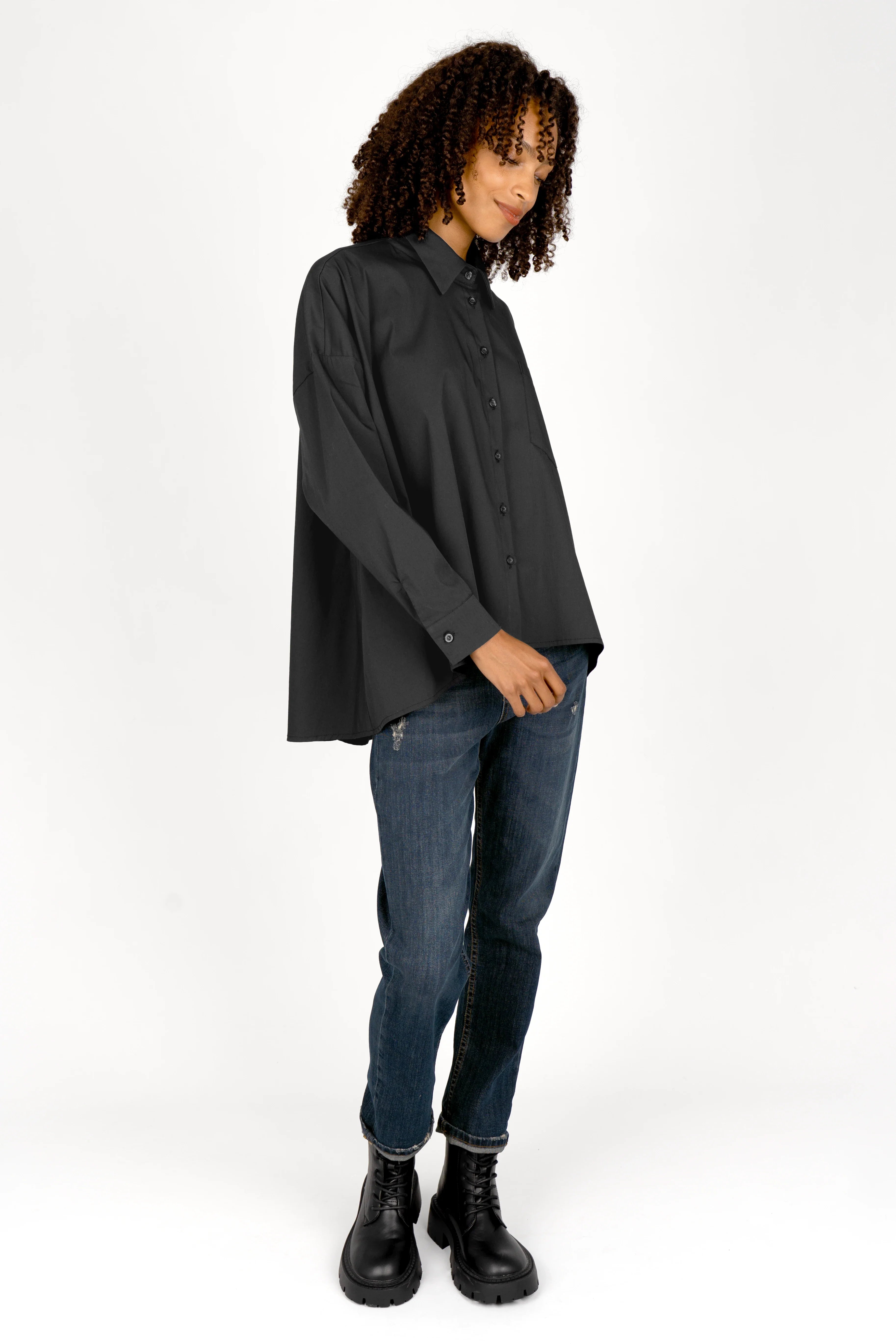 Woman wearing black oversized Bluse with classic collar, button front, and dropped shoulders paired with blue jeans and black boots