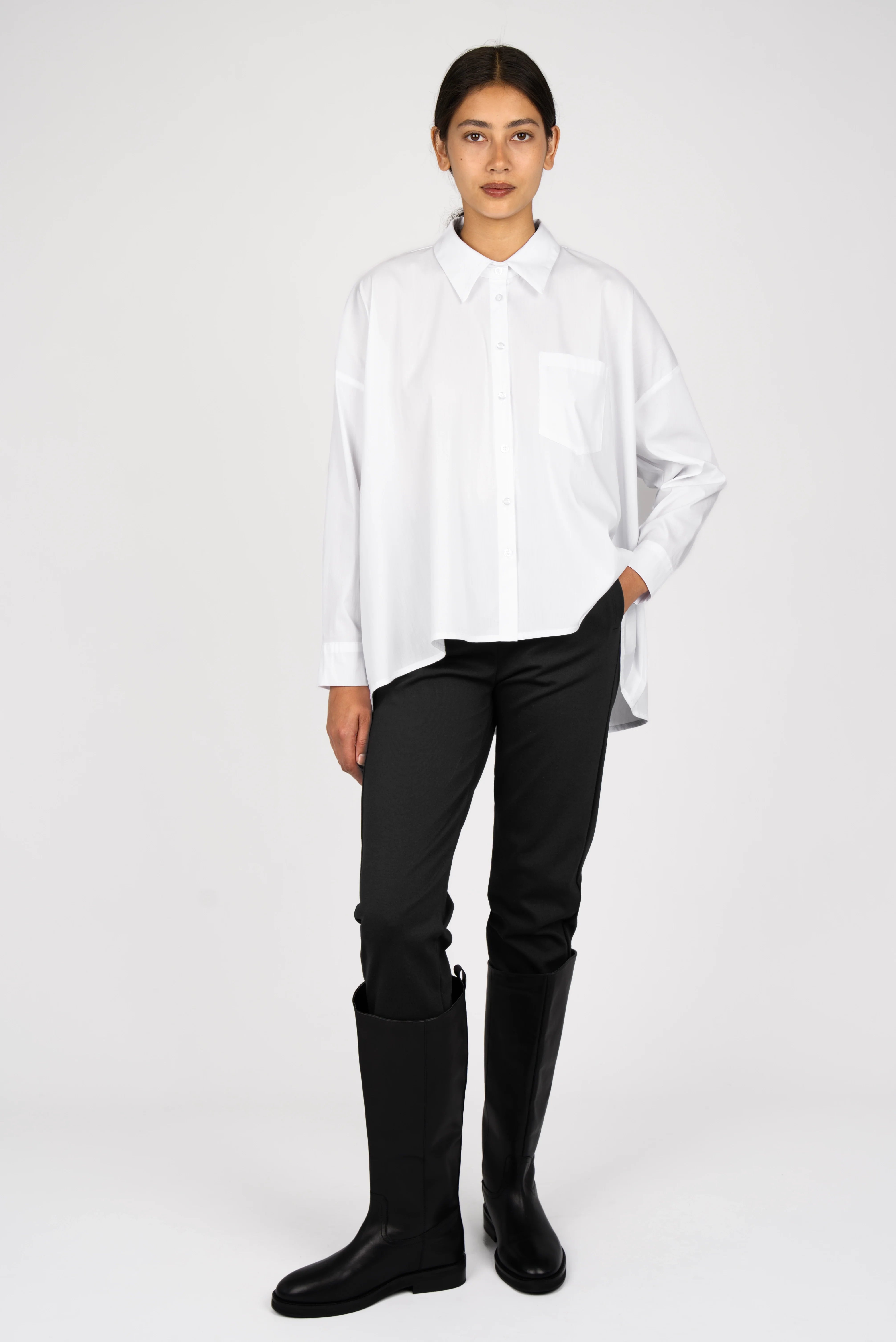 TIALY oversized white popeline blouse with A-line shape, classic collar, button front, and long sleeves styled with black pants and boots.