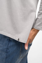Close-up of a light grey TIDA Blusenshirt Langarm with relaxed fit, V-neck, and long sleeves worn with blue jeans.