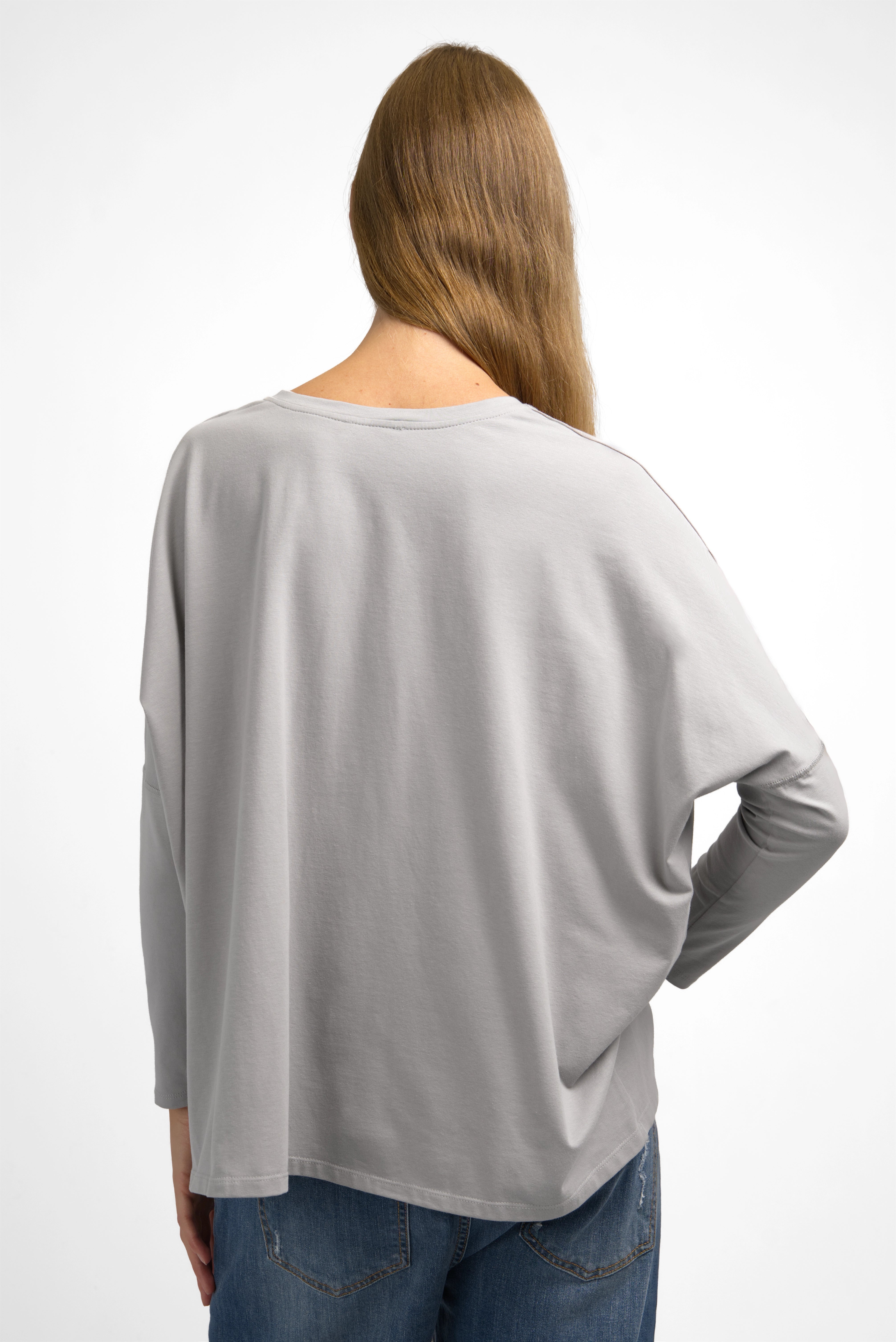 Back view of a woman wearing a relaxed fit TIDA Blusenshirt langarm in light gray with wide boxy shape and long sleeves