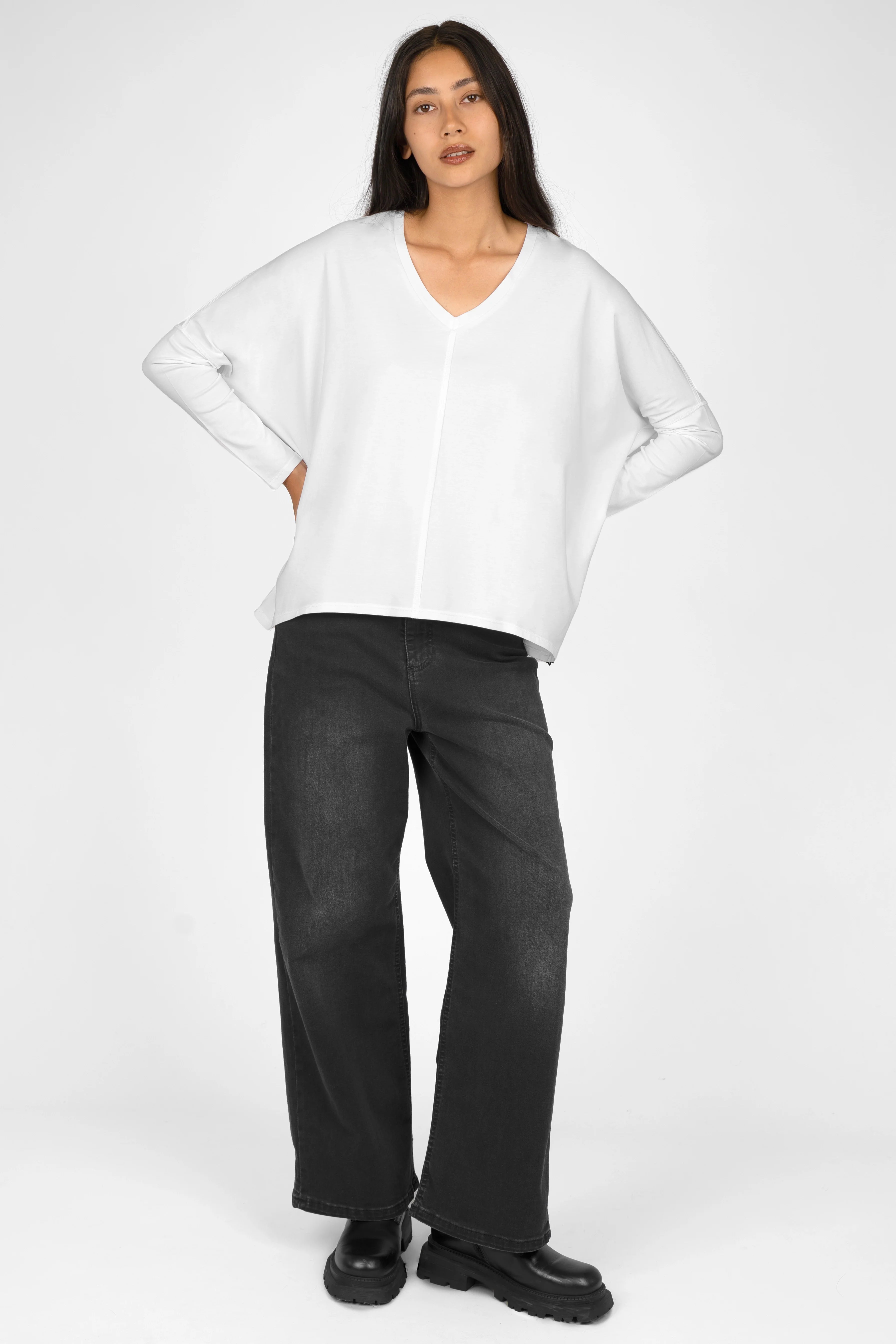Woman wearing white TIDA Blusenshirt Langarm with V-neck, relaxed fit, and long sleeves paired with black wide-leg pants.