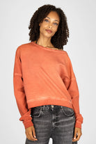 Woman wearing a burnt orange TIMAJ Revive One Shoulder Sweater with loose fit and wide neckline, paired with black denim jeans