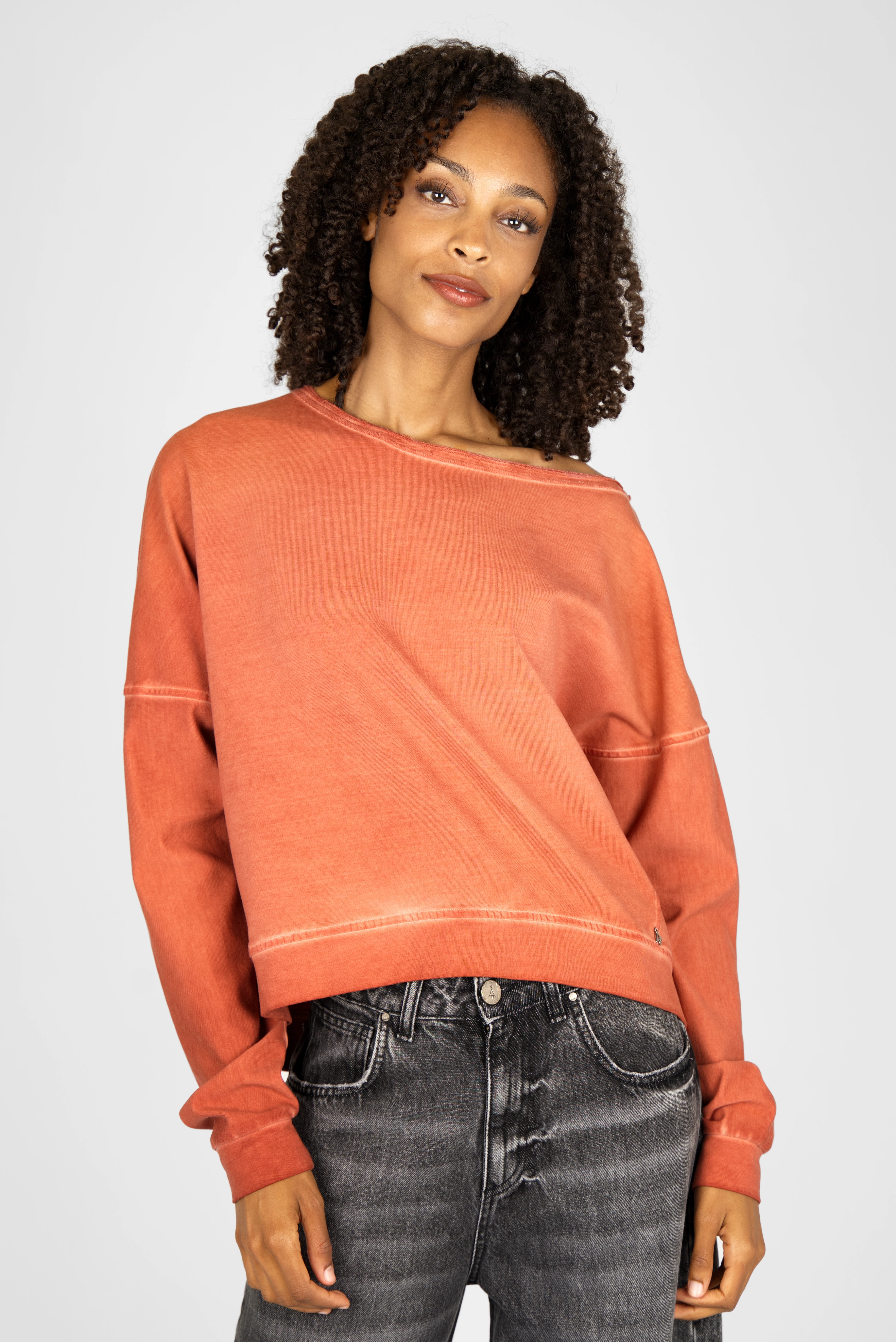 Woman wearing a burnt orange TIMAJ Revive One Shoulder Sweater with loose fit and wide neckline, paired with black denim jeans