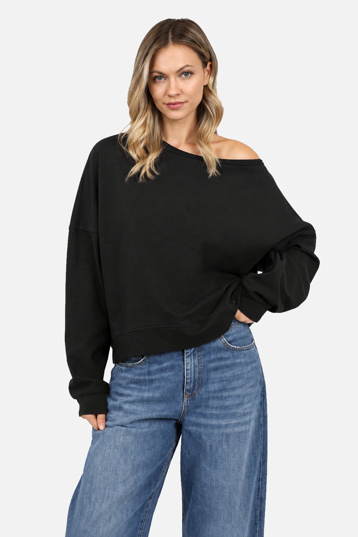 TIMAJ One Shoulder Sweater in Schwarz, Frontansicht mit blonder Frau und blauer Jeans, weiter Ausschnitt und entspannter Schnitt.