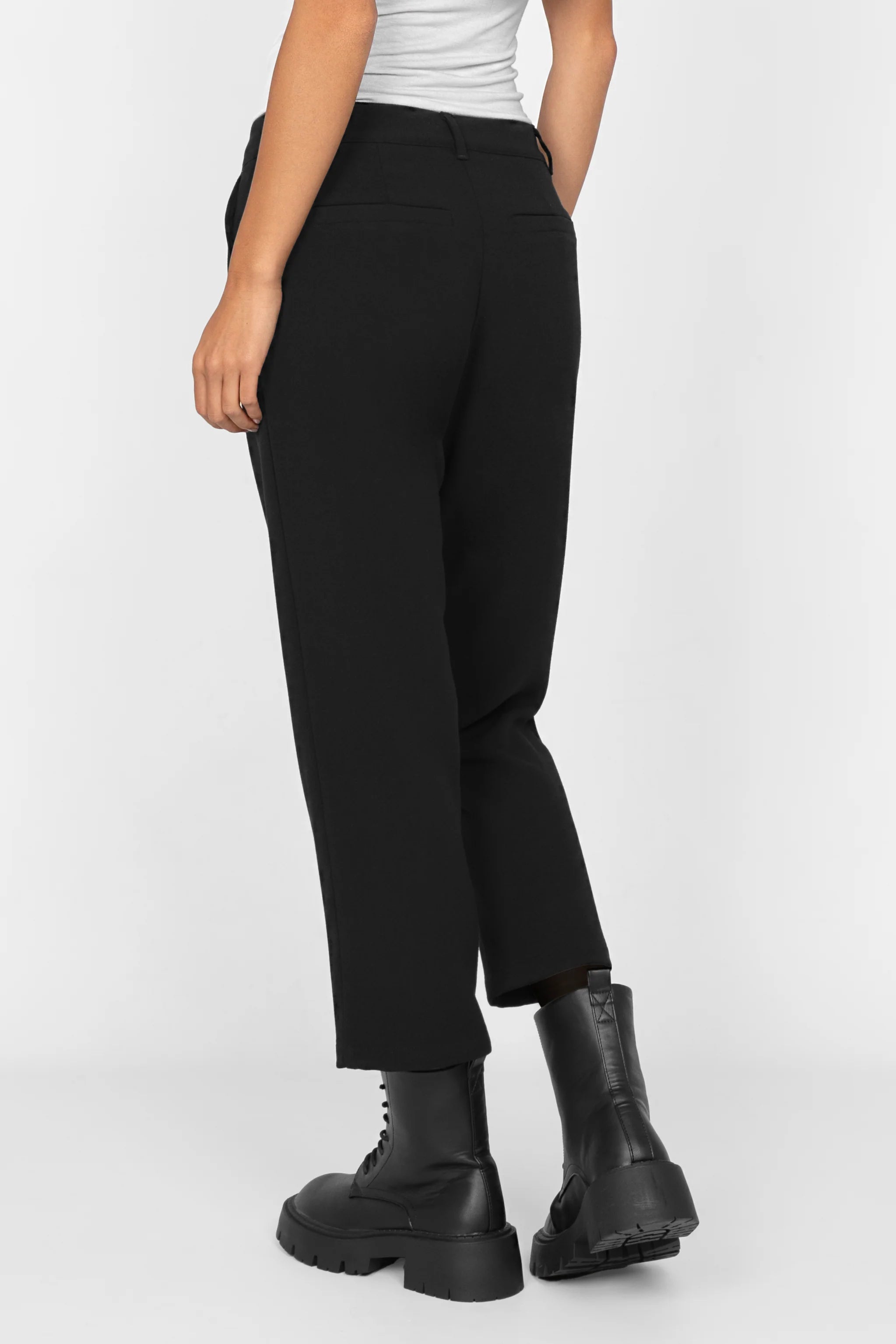 Back view of black cropped TINKE Hose Cropped fit pants with slight pleats, zip and button closure, worn with black boots