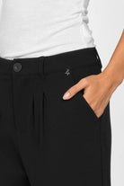 Close-up of black TINKE Hose Cropped fit pants with light pleats and button closure worn with white top