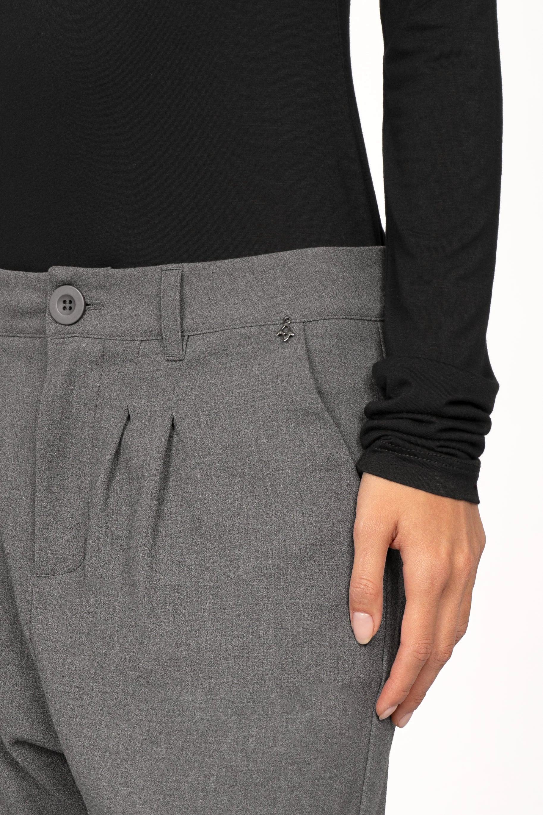 Close-up of gray TINKE Hose Cropped fit trousers with pleats and a button closure worn with a black long-sleeve top.