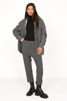 Woman wearing TINKE Hose Cropped grey cropped pants with pleats, styled with black turtleneck and grey jacket.