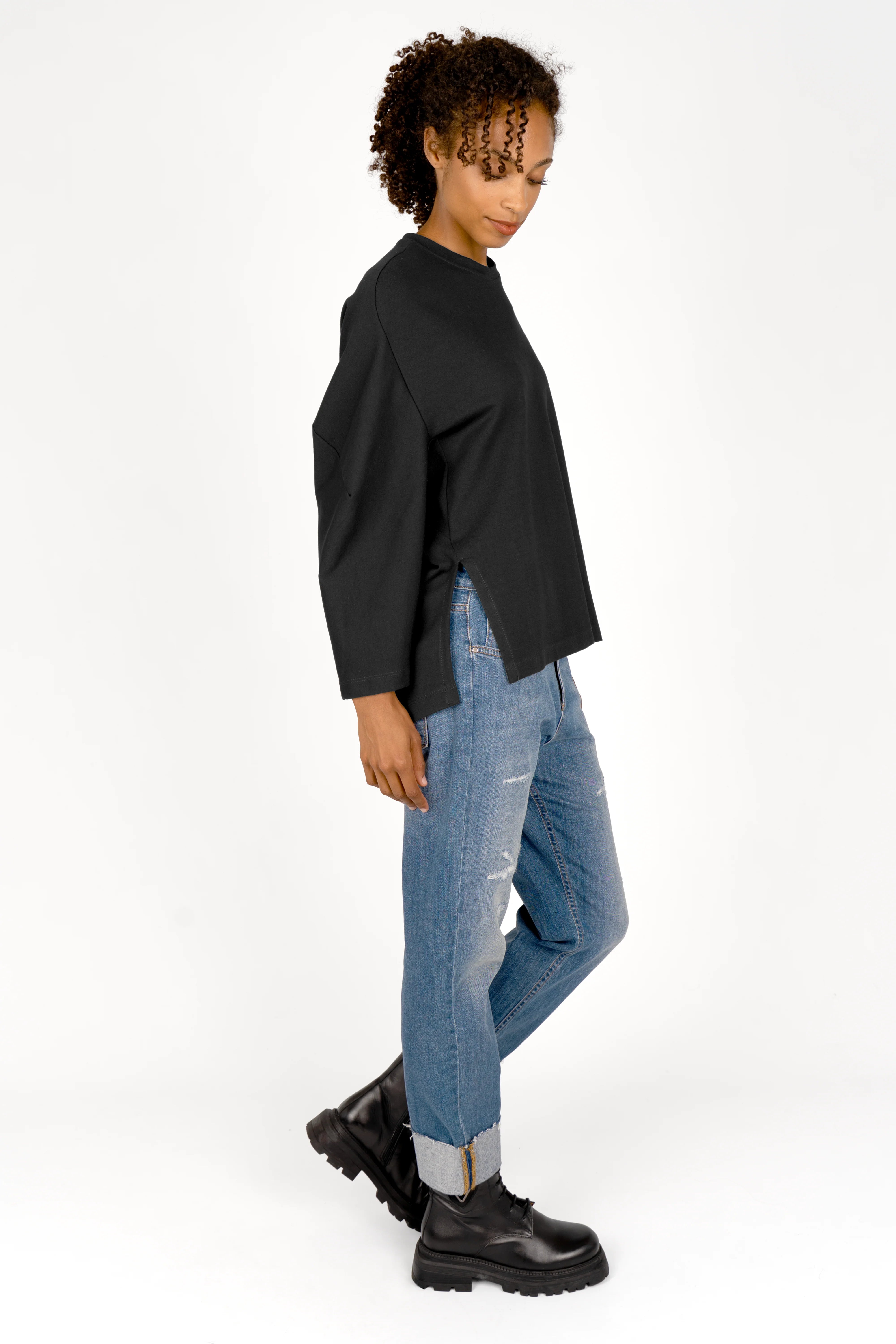 Woman wearing black TOOVE Shirt in relaxed fit with curved seams and high side slits paired with cuffed blue jeans and black boots