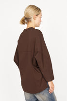 Damen trägt braunes TOOVE Shirt aus mittelschwerem Interlock-Jersey mit verlängertem Rücken und geschwungenen Teilungsnähten, Rückansicht.