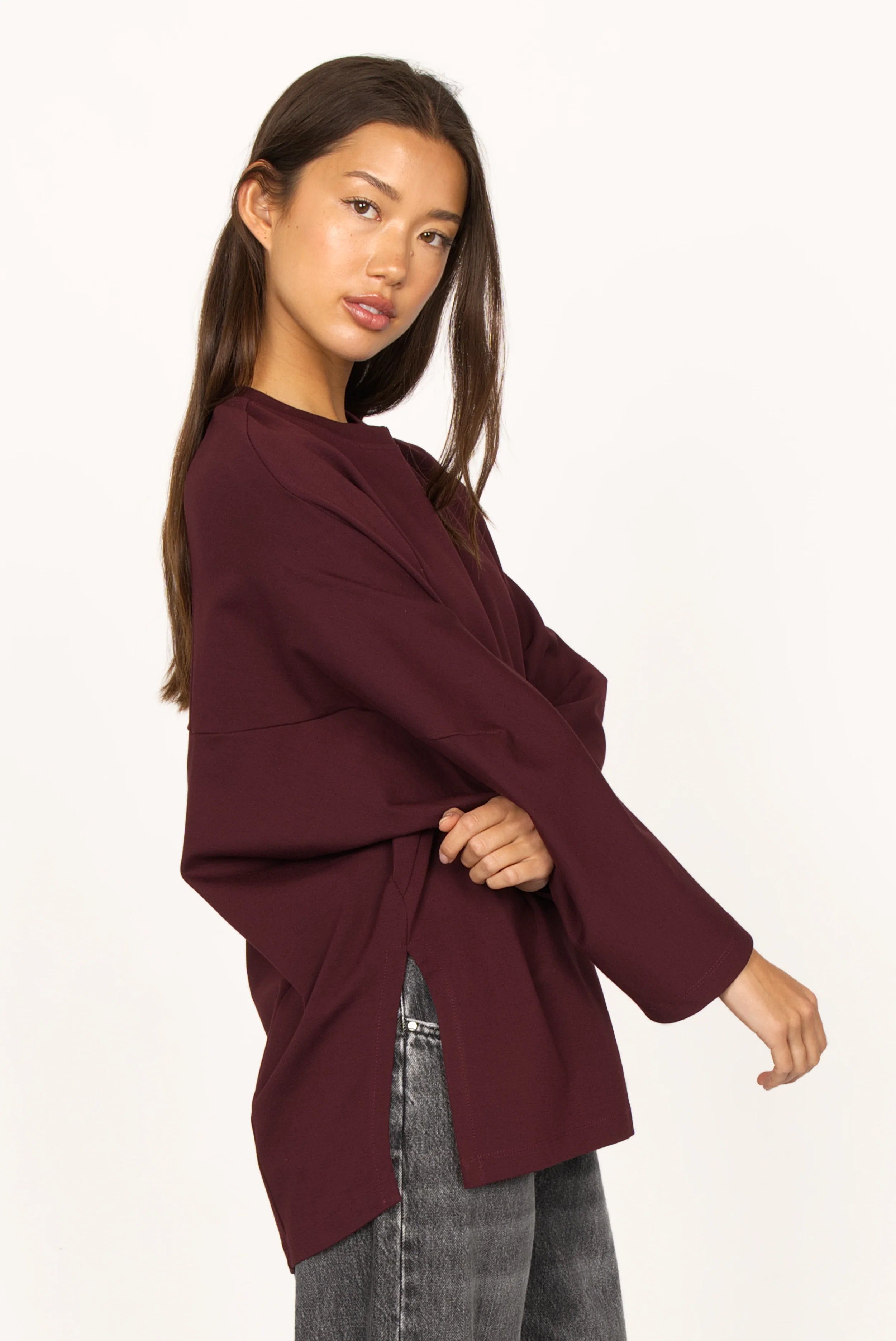 Woman wearing a relaxed fit TOOVE Shirt in dark burgundy interlock-jersey with extended back and high side slits.