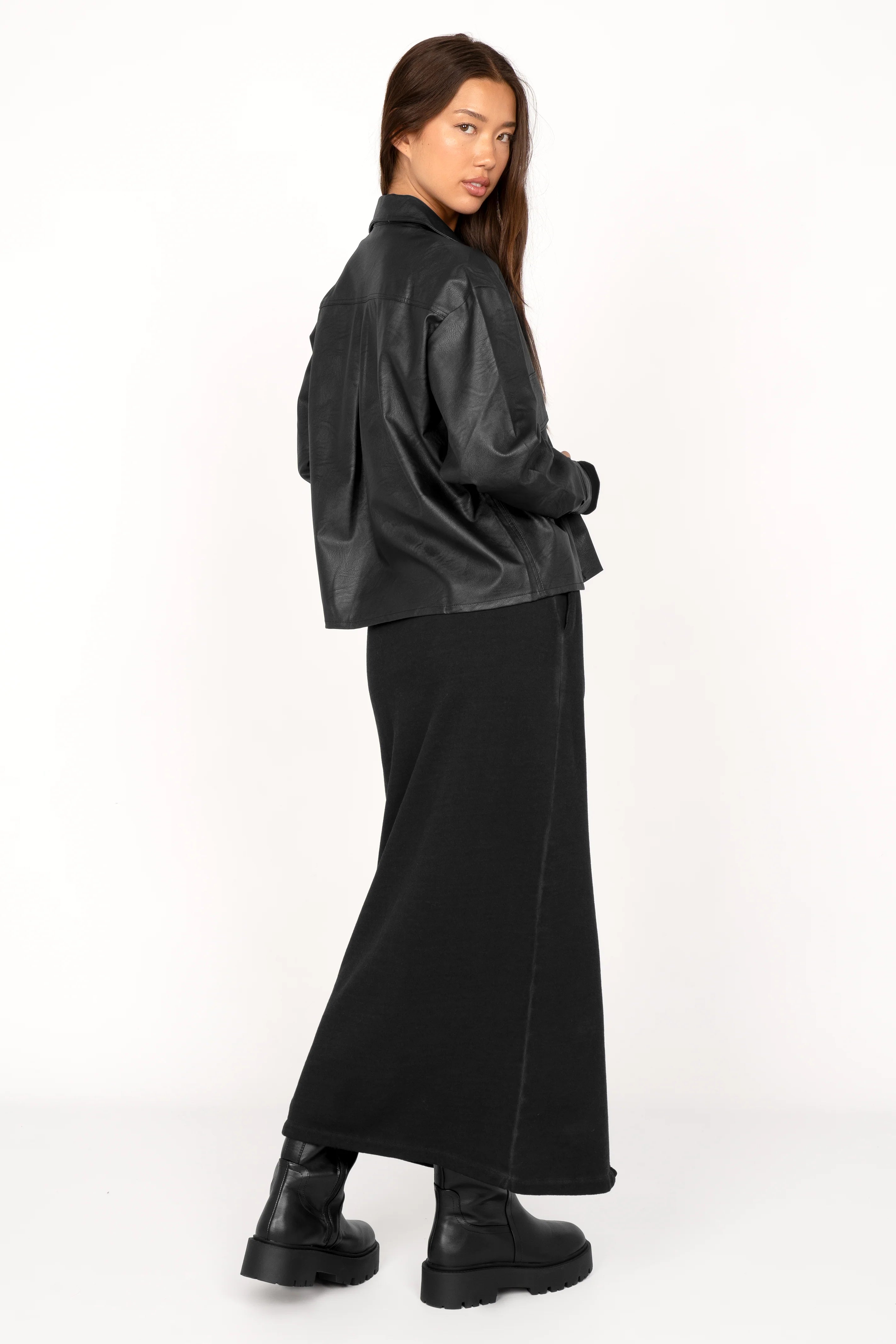 Woman wearing a cropped black Hemdjacke aus supersoftem Eco-Leder with Kent collar and chest pockets, styled with a long black skirt and boots.