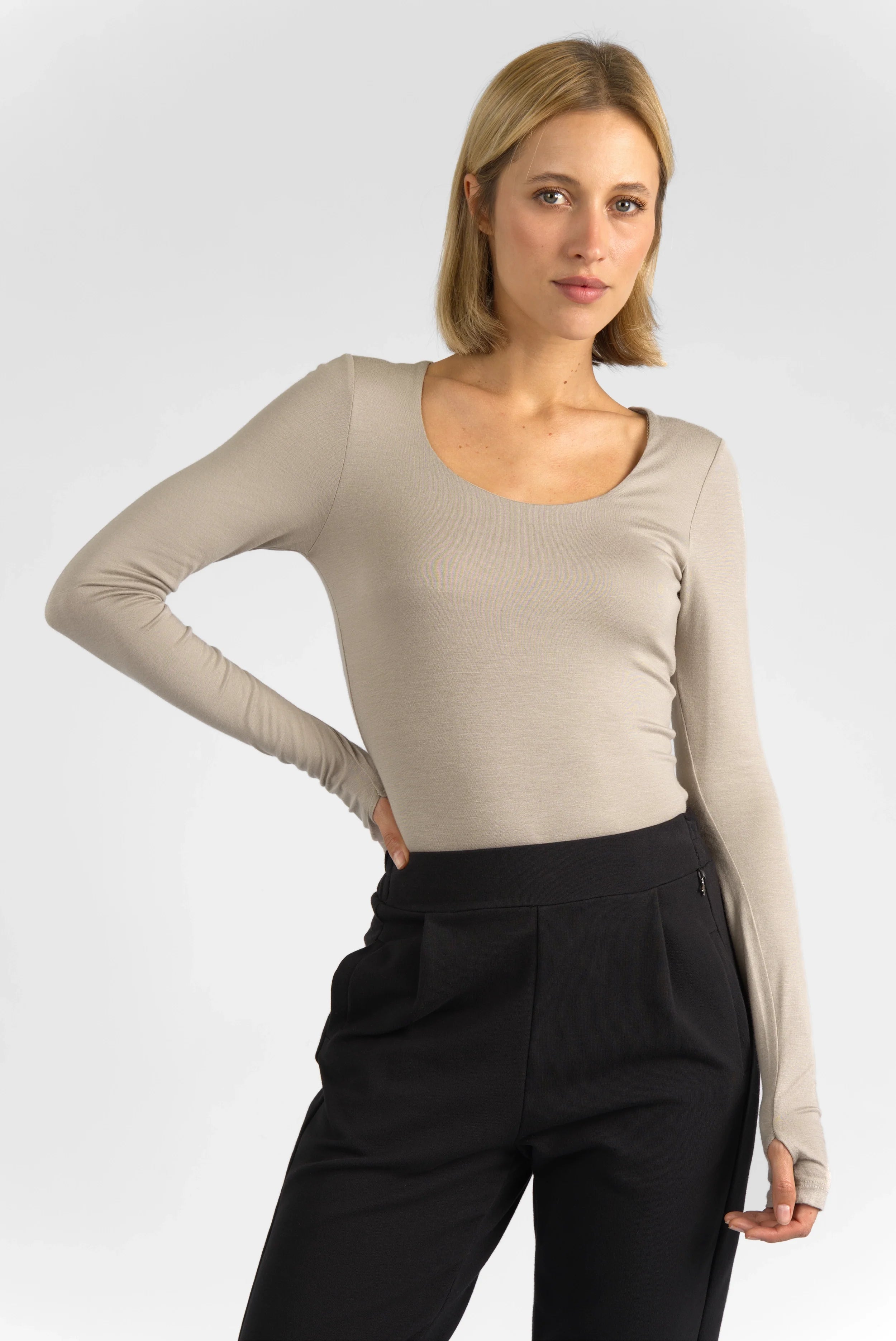 Damen trägt VALUM Longsleeve in Beige mit U-Boot Ausschnitt und Daumenlöchern, kombiniert mit schwarzer Hose