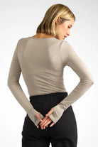 Woman wearing beige VALUM Longsleeve with U-boat neckline, extra-long sleeves, and thumbholes, styled with black pants