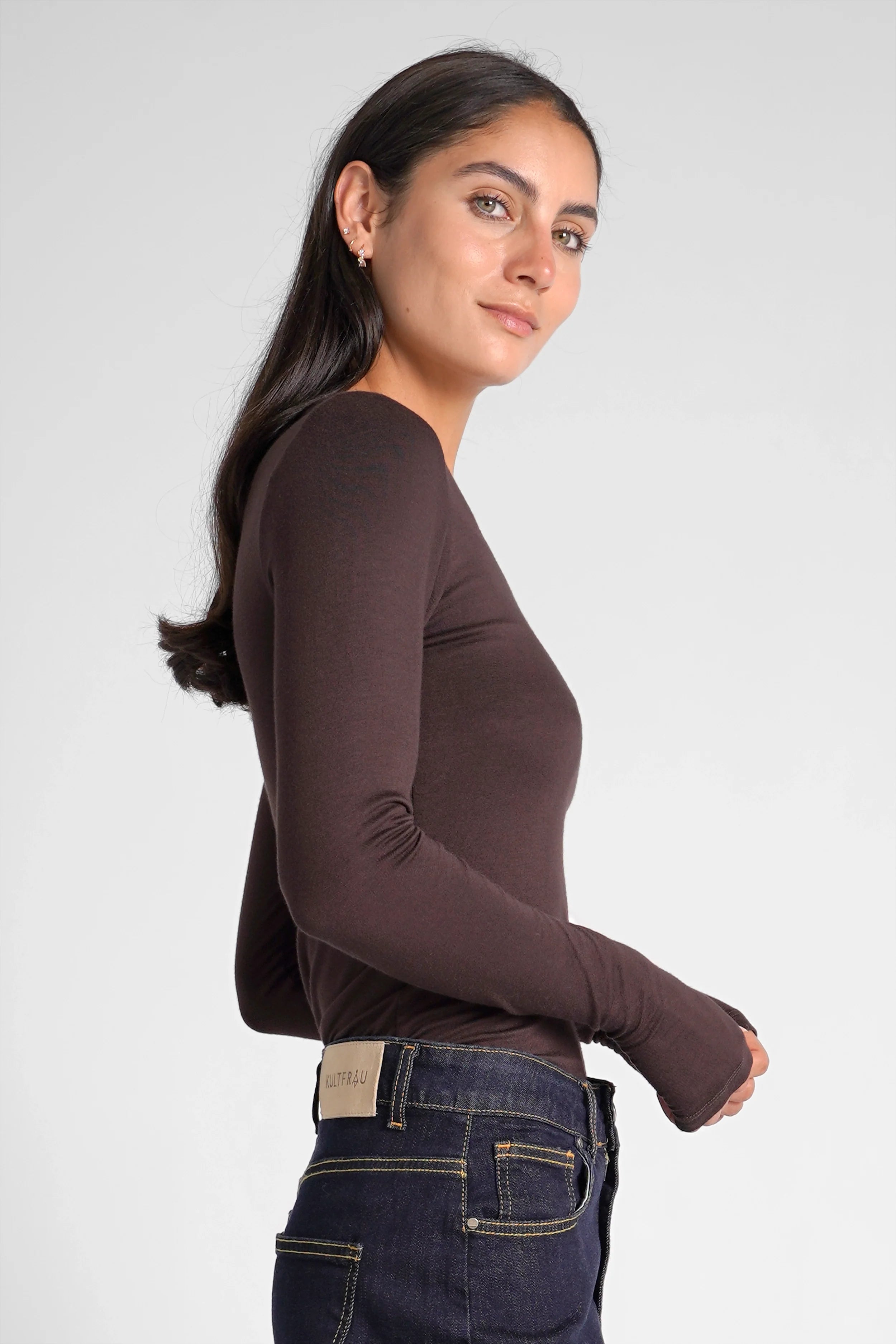 Woman wearing a slim fit VALUM Longsleeve with U-boat neckline and extra long sleeves with thumb holes in dark brown color.