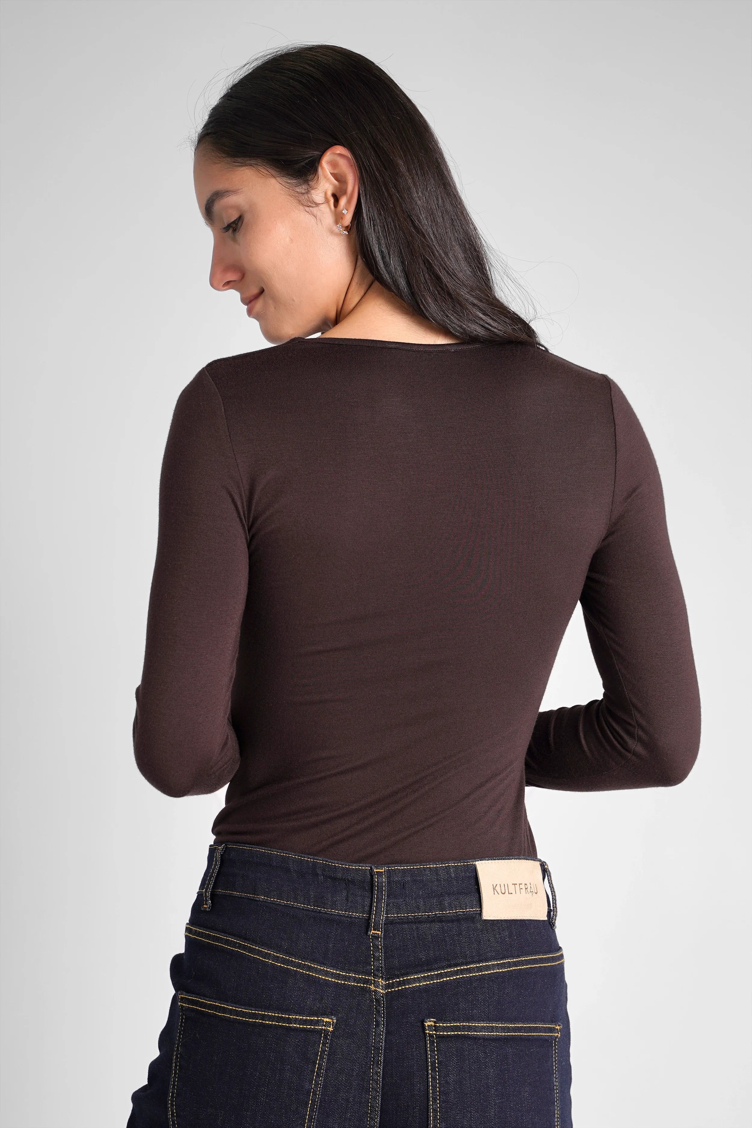 Back view of woman wearing slim fit VALUM Longsleeve with extra long sleeves and thumbholes in dark brown