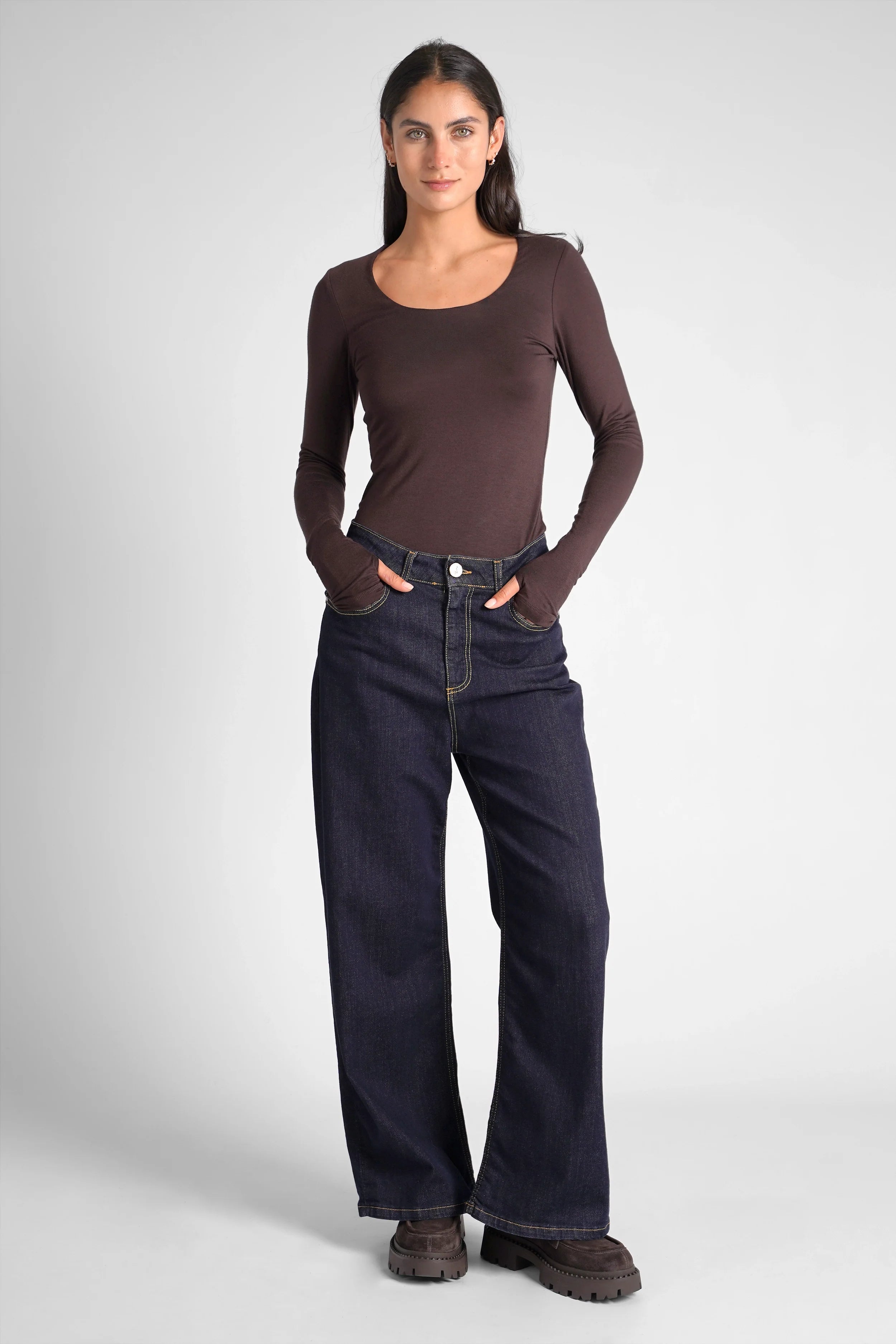 Woman wearing a slim fit VALUM Longsleeve with U-boat neckline, extra long sleeves with thumb holes, paired with dark wide-leg jeans.