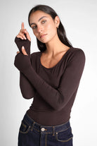 Woman wearing a slim fit VALUM Longsleeve with U-boat neckline and extra long sleeves with thumb holes in dark brown.
