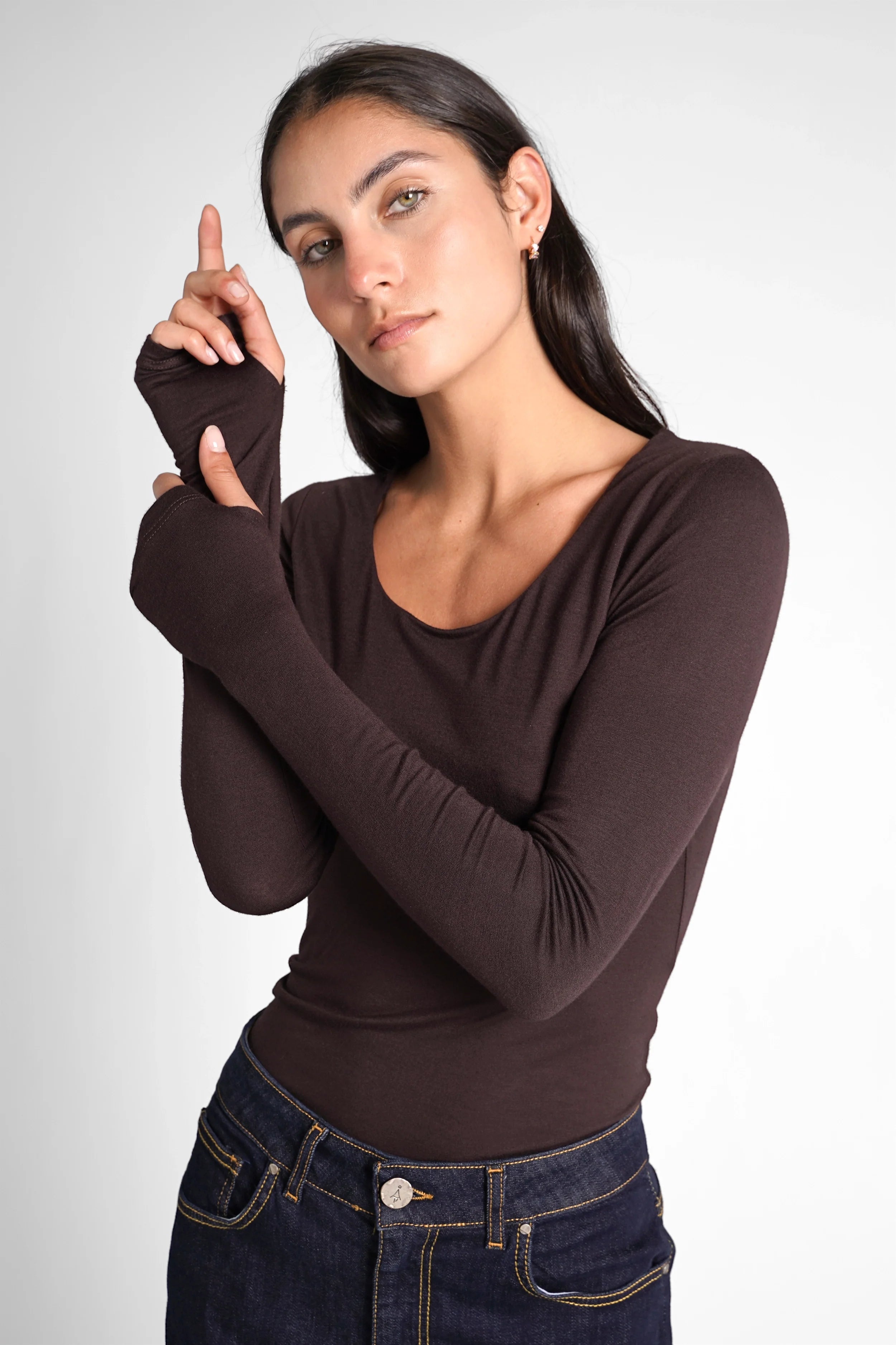 Woman wearing a slim fit VALUM Longsleeve with U-boat neckline and extra long sleeves with thumb holes in dark brown.