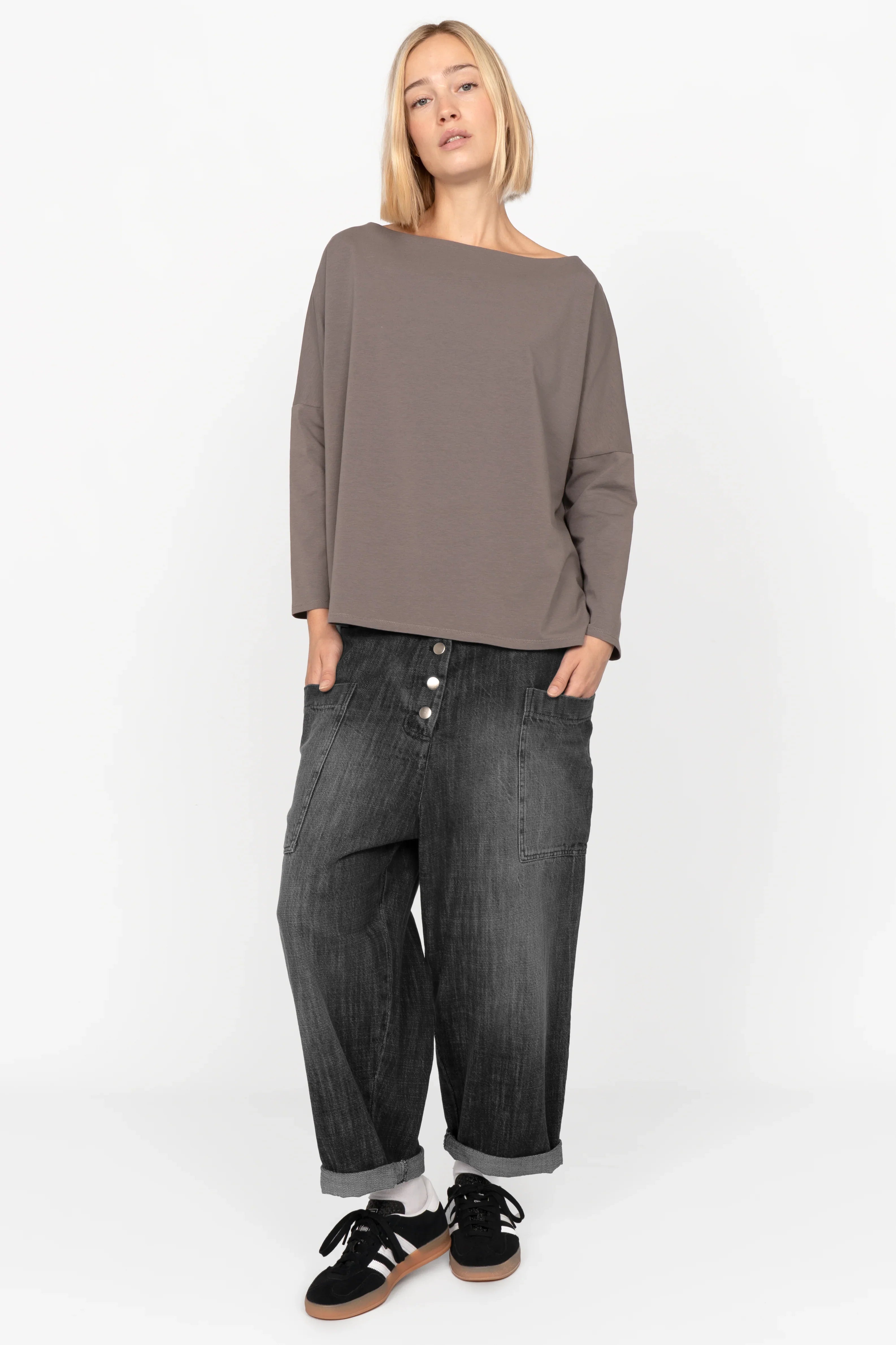 Female model wearing VIKADA Revive Baggy Hose in black denim with button fly and side pockets, styled with relaxed fit and rolled-up cuffs.