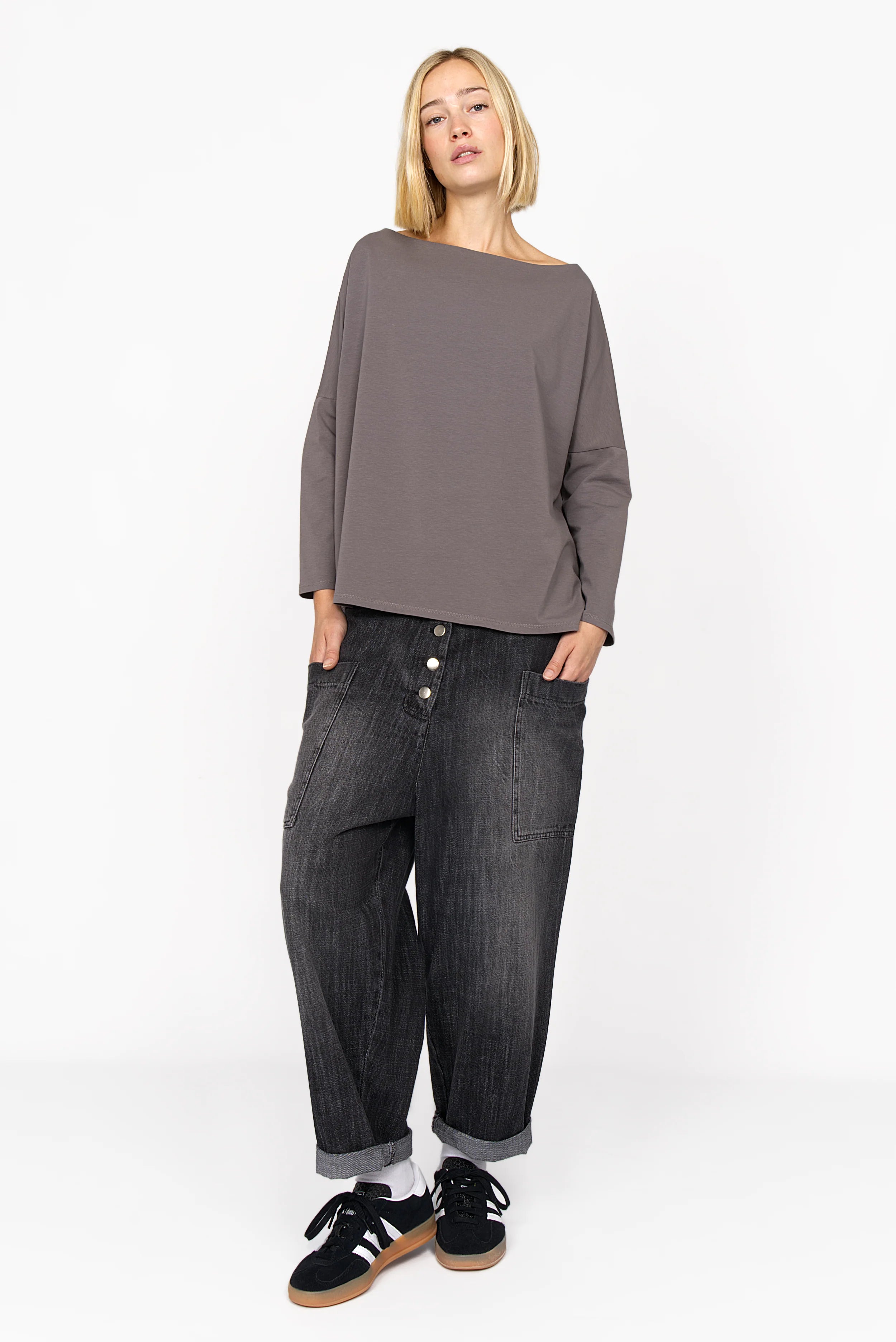 Damen trägt VIKADA Revive Baggy Hose aus strukturierter Baumwolle mit weitem Schnitt und markanter Knopfleiste in dunkelgrauer Denim-Optik.