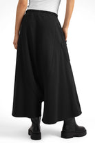 Black radially wide Hosenrock aus Sweat with asymmetrical front pocket and smooth waistband worn with black boots.