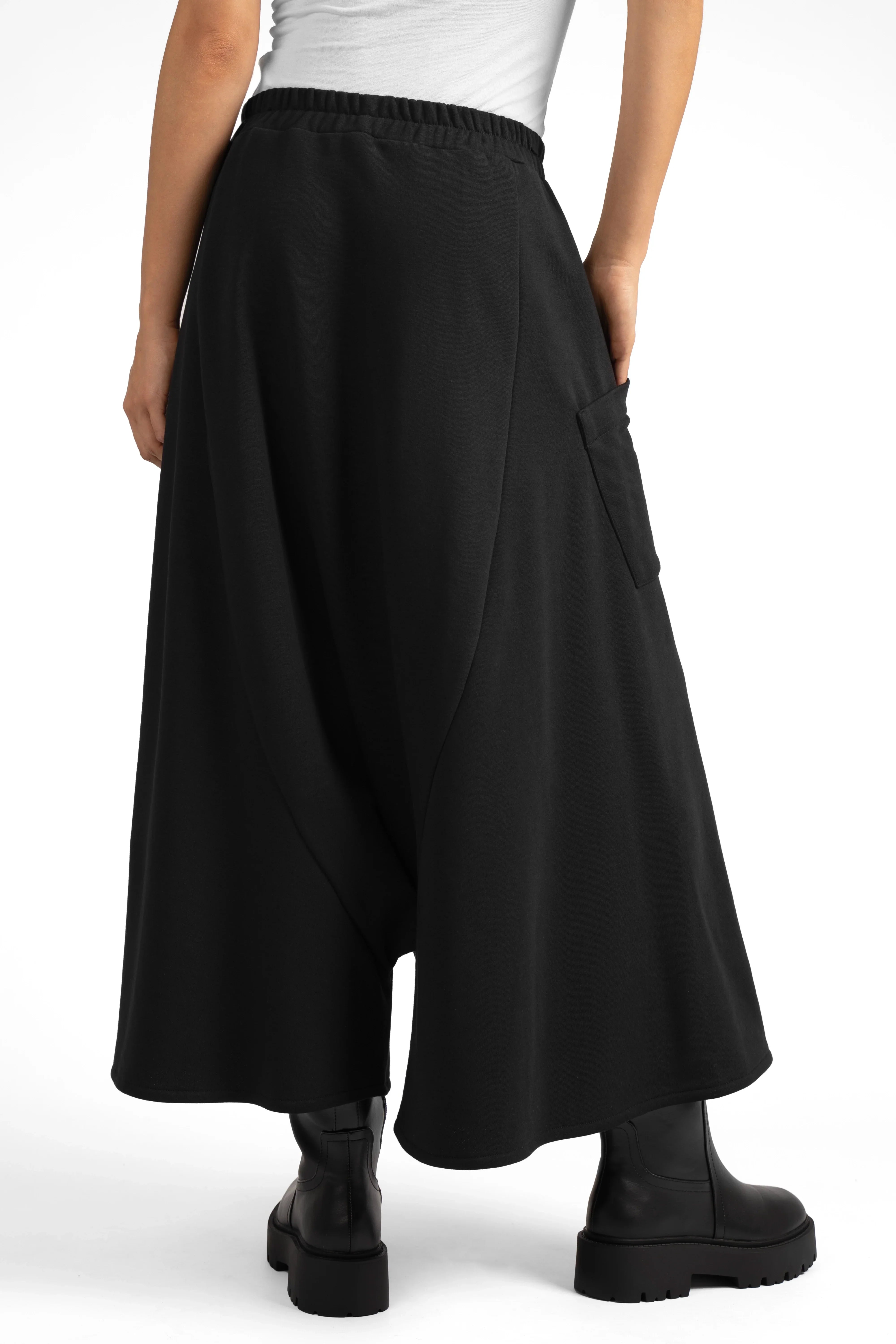 Black radially wide Hosenrock aus Sweat with asymmetrical front pocket and smooth waistband worn with black boots.