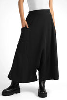Black radially wide Hosenrock aus Sweat with asymmetrical front pocket and smooth waistband, styled with black boots.
