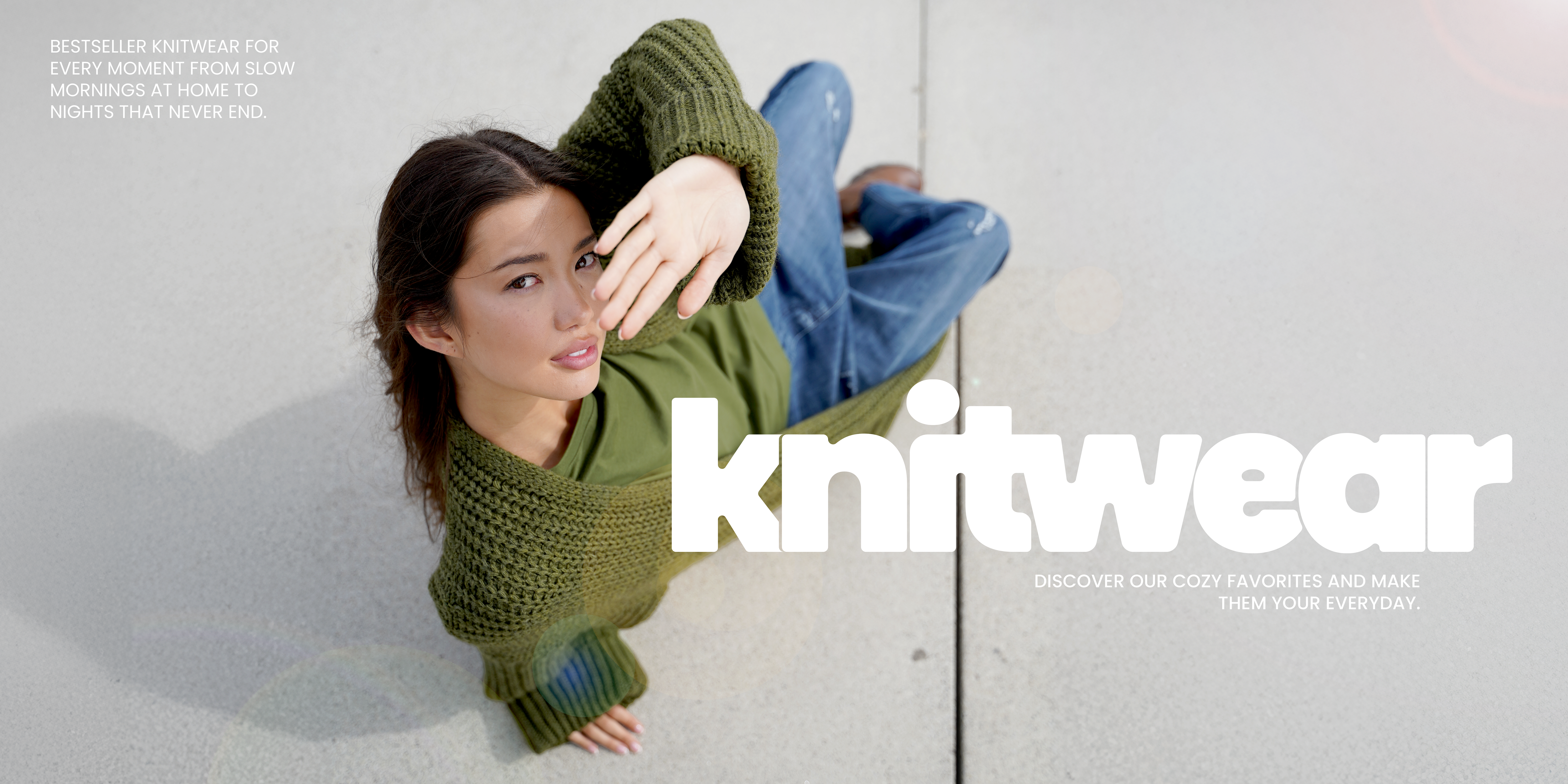 Eine Frau sitzt entspannt auf dem Boden, trägt ein olivgrünes Strick-Cardigan über einem grünen Oberteil und einer blauen Jeans. Sie schützt ihr Gesicht spielerisch vor der Sonne. Dazu der Text „Knitwear – Discover our cozy favorites and make them your everyday“, der die Strickmode als Alltagsfavoriten inszeniert.